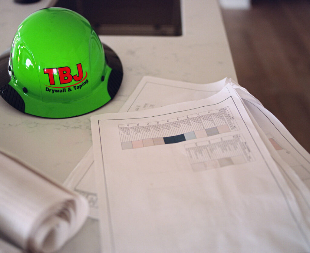 green tbj hardhat sitting on blueprints